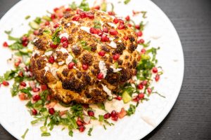 whole baked cauliflower served on a bed of salad and tahini sauce