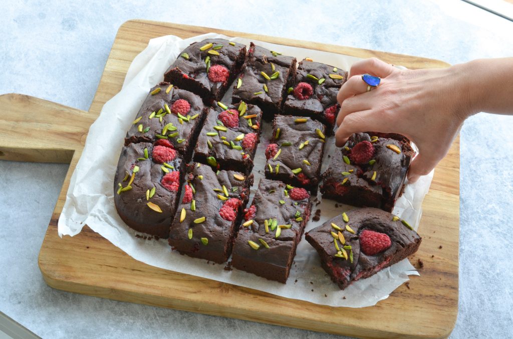 raspberries and pistachio brownie served on a wooden board
